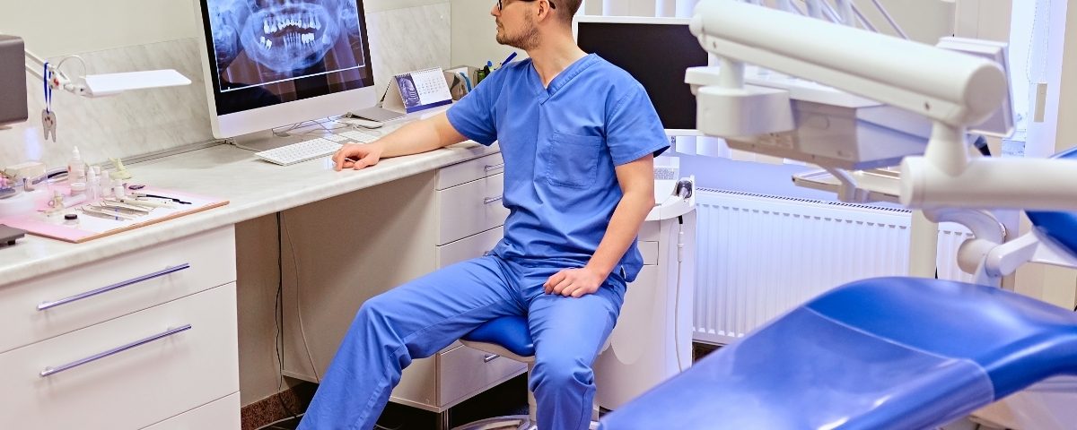 Dentist at a surgery workstation with a dental X-ray on screen