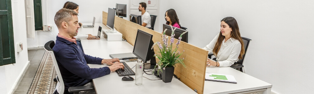 Office team working at desktop computers in a shared workspace, highlighting traditional IT setups compared to modern remote and hybrid working environments